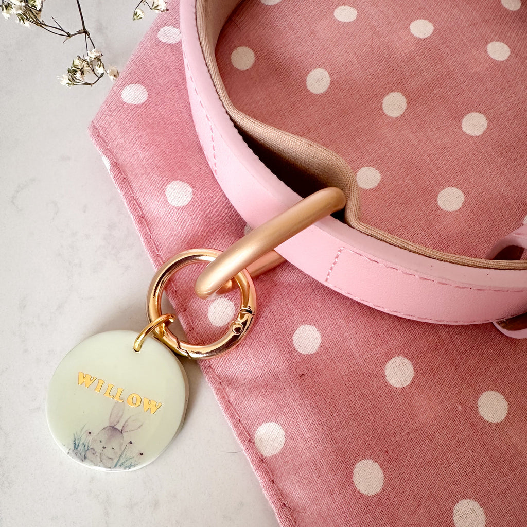 Pink polka dot bag with a gold handle and decorative pet id tag on a light background