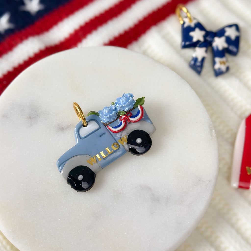 Decorative pick with a vintage truck and flowers on a marble surface with an American flag in the background.